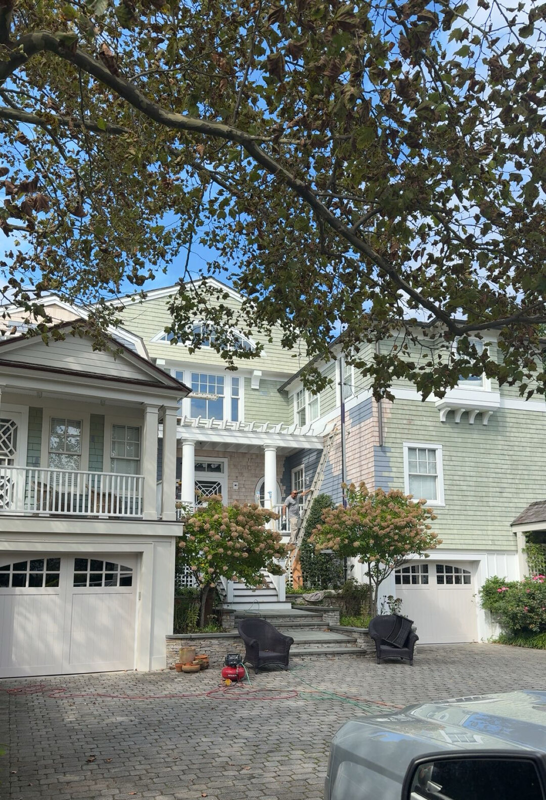 A large shingle-style home in Monmouth County with fresh siding and white trim, framed by autumn trees.