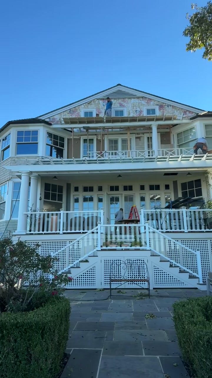 White shingle-style coastal home mid-renovation with new exterior work.