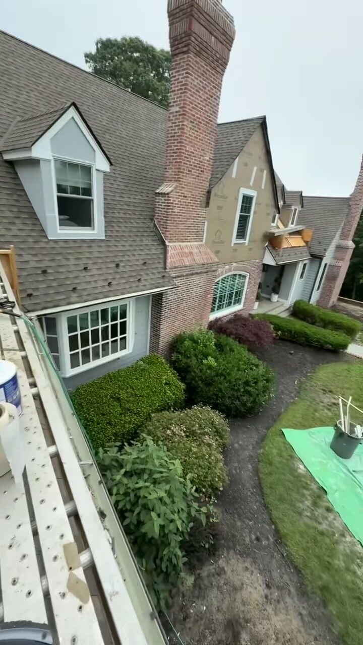 Brick Tudor-style home with chimney and landscaped grounds during exterior work.